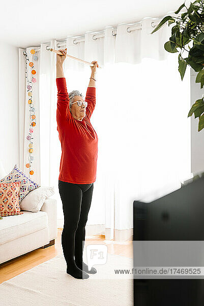 Frau mit erhobenen Armen übt zu Hause Gymnastik