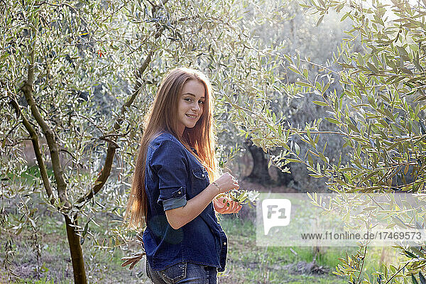 Smiling young woman with long hair amidst olive trees at countryside