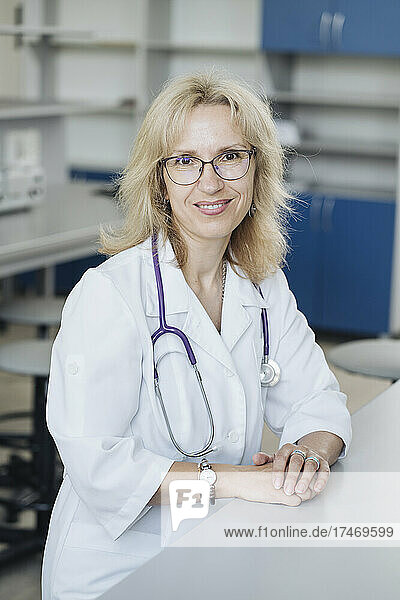 Smiling blond doctor with stethoscope at desk