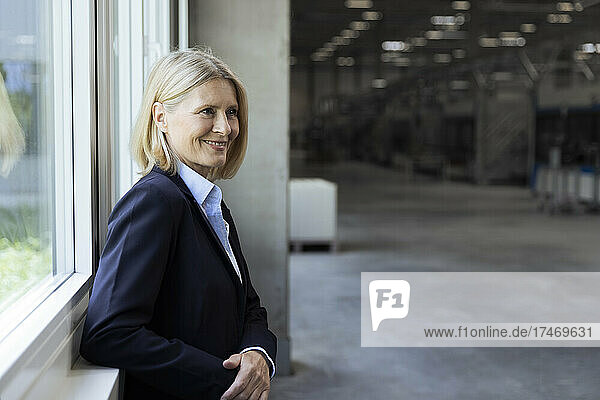 Smiling blond businesswoman standing at window in industry
