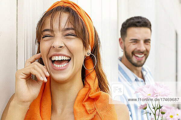 Woman laughing while man standing with flowers in background by wall