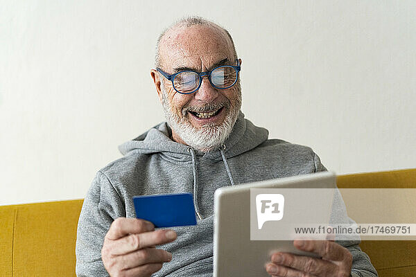 Bearded senior man doing online shopping through tablet PC at home