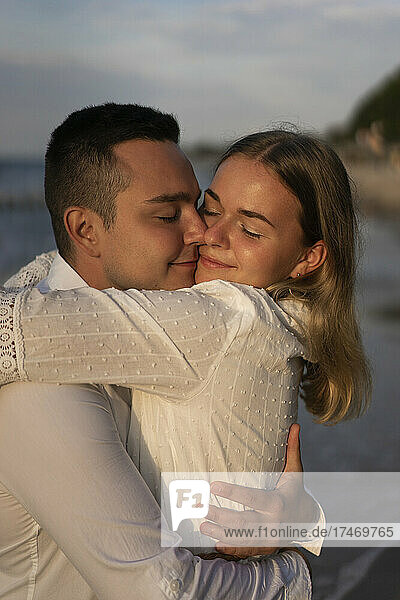 Smiling couple with eyes closed embracing at beach