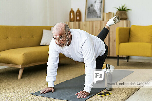 Fit senior man practicing Bharmanasana yoga pose at home