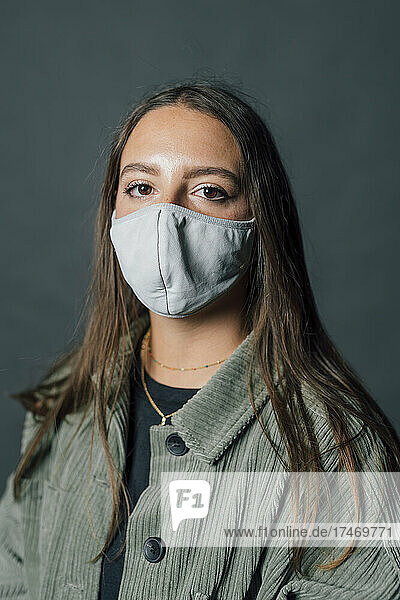 Woman with long hair wearing protective face mask against gray background