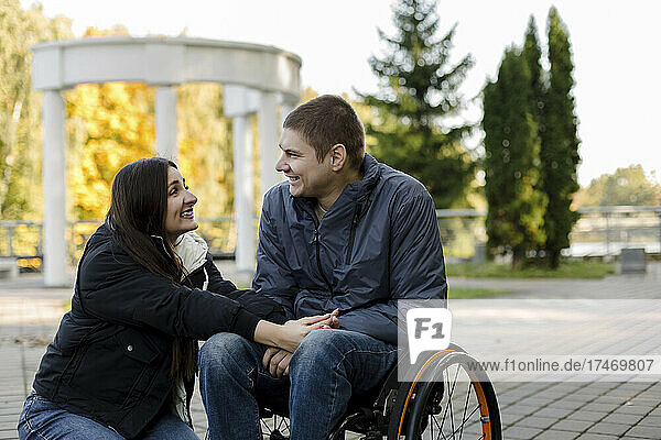Girlfriend smiling at boyfriend sitting in wheelchair in park