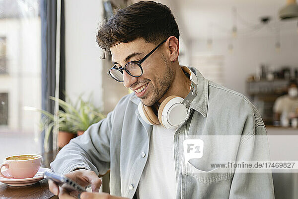 Smiling businessman with eyeglasses using mobile phone in cafe