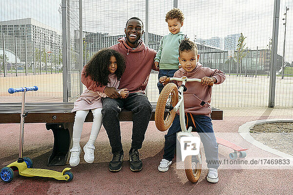 Happy father sitting with arm around children at sports field