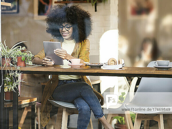 Smiling woman with afro hairstyle using tablet PC at cafe window