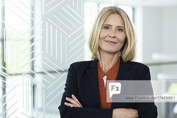 Confident blond female professional standing with arms crossed in office