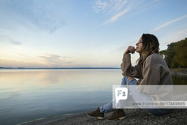 Nachdenkliche Frau sitzt auf einem Felsen und blickt auf den See