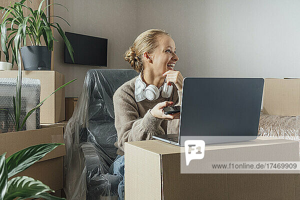 Smiling woman with laptop and mobile phone at new home