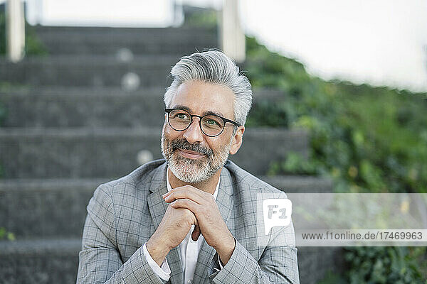 Thoughtful businessman with eyeglasses sitting on steps