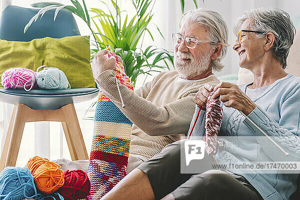 Senior man showing knitted wool to woman at home