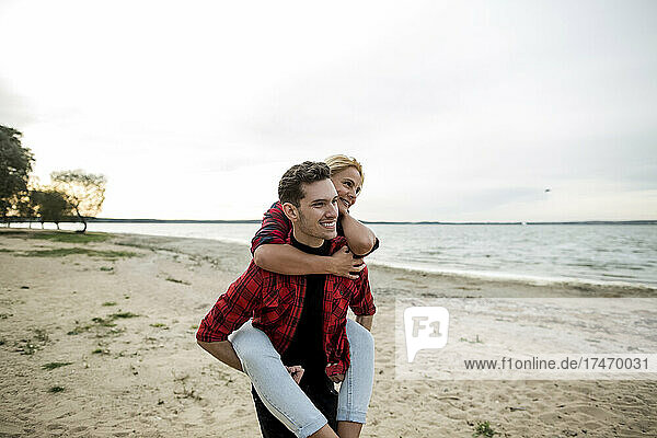 Smiling boyfriend giving piggyback ride to girlfriend at beach