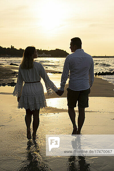 Boyfriend and girlfriend holding hands while walking at beach on sunset