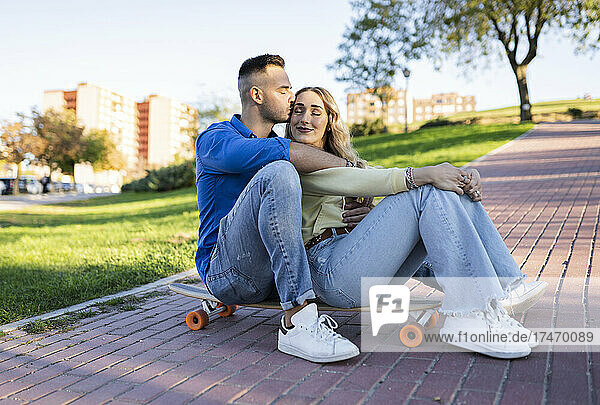 Boyfriend kissing girlfriend on skateboard at park