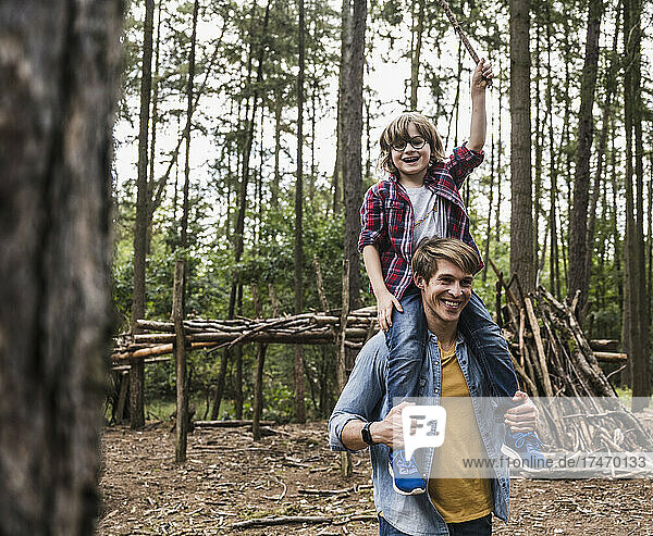 Happy man carrying son on shoulders in forest