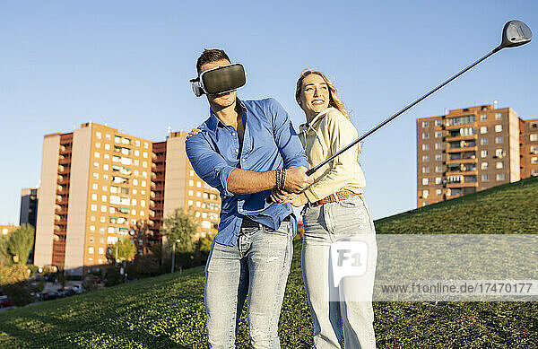 Man with virtual reality headset playing golf by girlfriend on hill