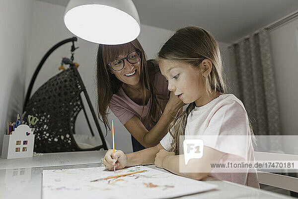 Mother looking at daughter painting on paper