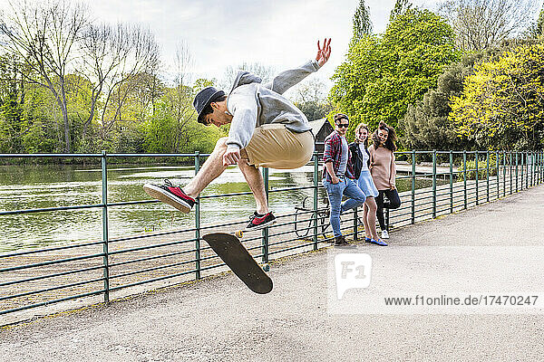 Young man showing stunt on skateboard to friends in park