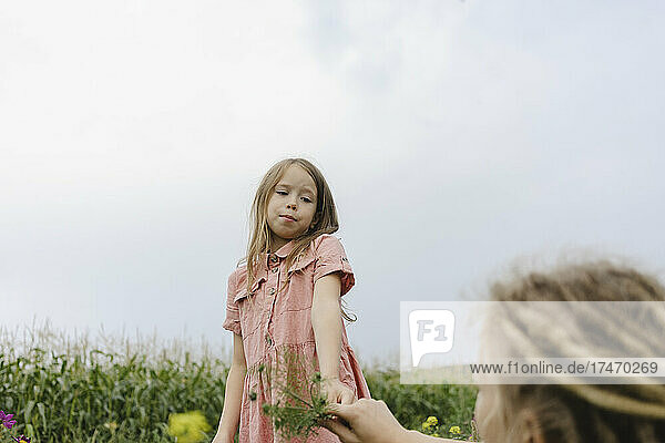 Girl holding plant looking at mother in corn field