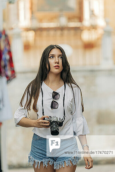 Young woman contemplating holding digital camera
