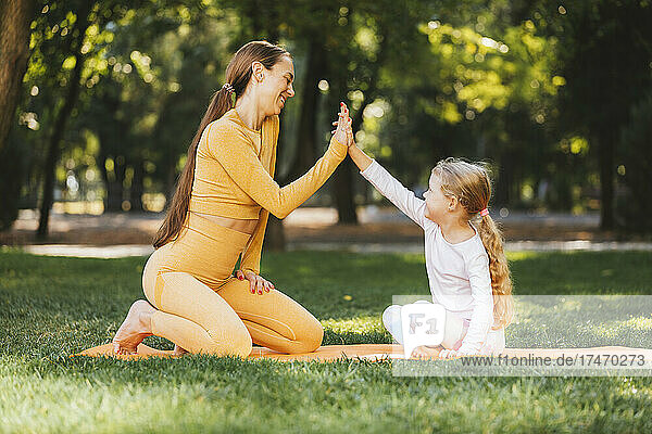 Smiling girl giving high-five to mother in public park