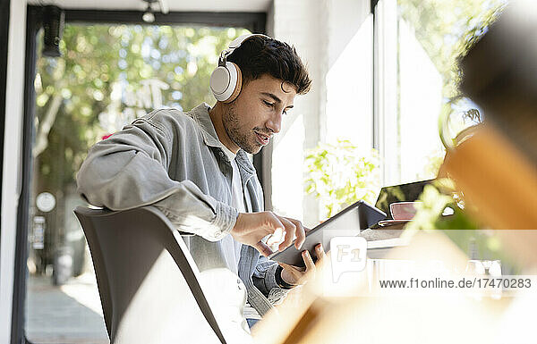 Businessman with headphones using tablet PC in coffee shop