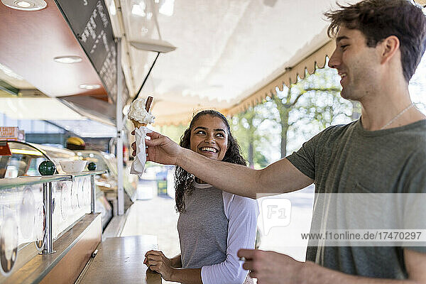 Smiling woman looking at friend buying ice cream at park