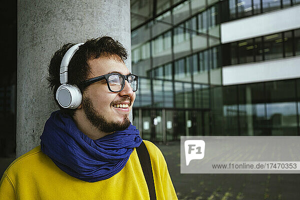 Lächelnder Student  der auf dem Universitätscampus Musik über Kopfhörer hört