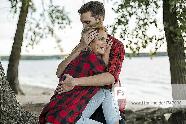 Junger Mann umarmt lächelnde Freundin am Strand