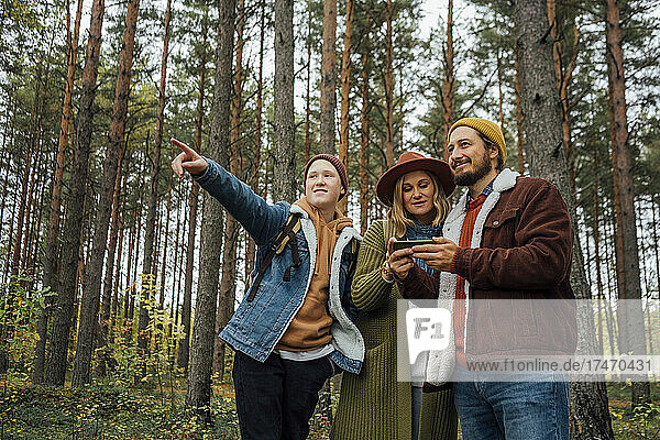 Boy pointing while parents using smart phone in forest