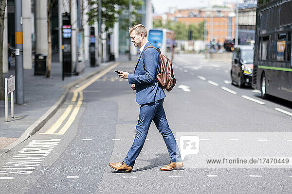 Businessman using mobile phone while crossing road