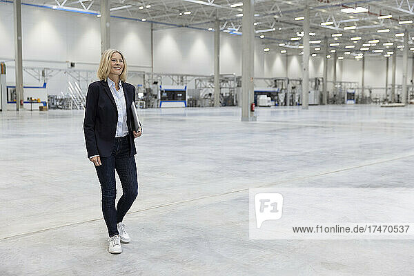Smiling female professional with laptop walking in industry