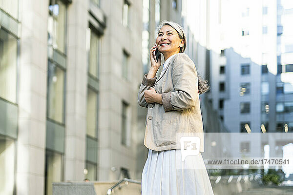 Mature woman smiling while talking on smart phone in city