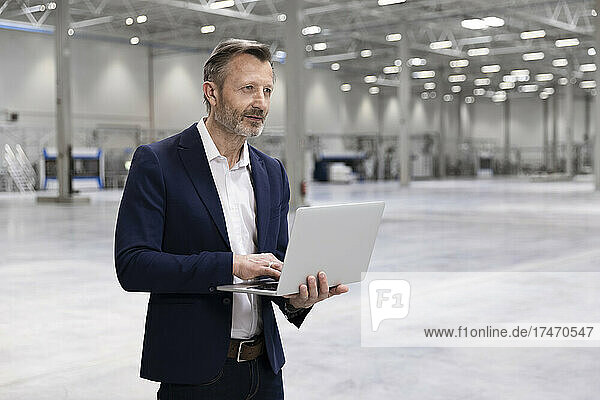 Male professional standing with laptop in factory