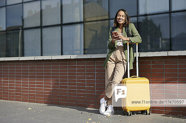 Happy woman with mobile phone leaning on luggage
