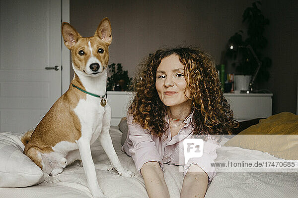 Smiling woman lying on bed with dog in bedroom