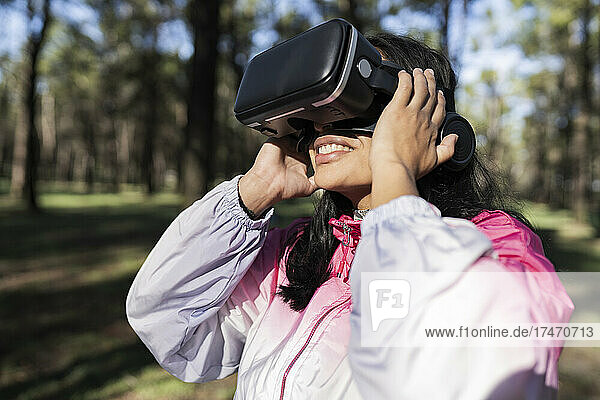 Frau schaut an einem sonnigen Tag durch ein Virtual-Reality-Headset im Park zu