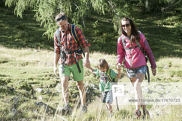 Happy parents holding hands of son while hiking on alpine meadow during vacation