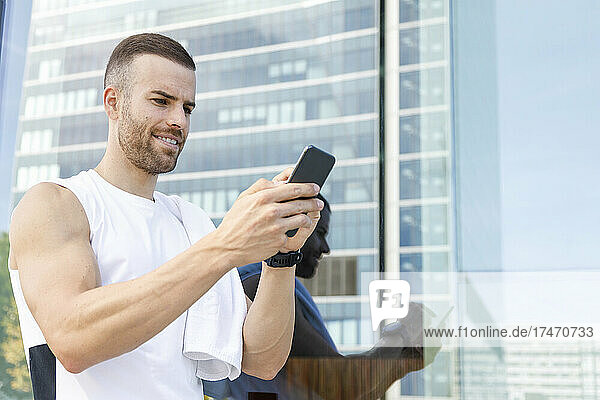 Male athlete using smart phone by glass wall