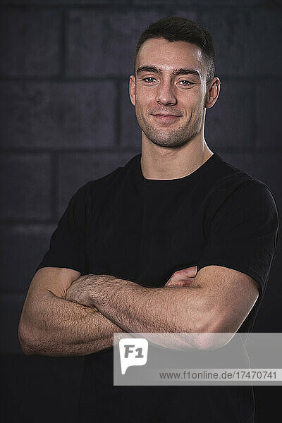 Smiling male athlete with arms crossed standing in front of wall