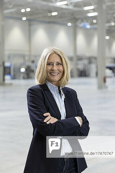 Smiling blond businesswoman standing with arms crossed in factory