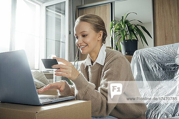 Smiling woman with credit card paying online through laptop at home