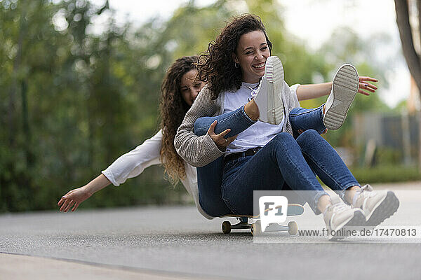 Fröhliche junge Freundinnen haben Spaß beim Skateboarden im Park