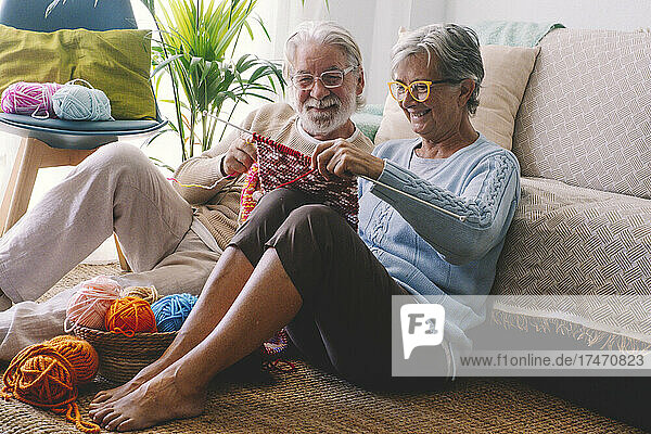 Smiling senior couple knitting wool together in living room