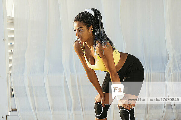 Tired female athlete looking away while bending on sunny day