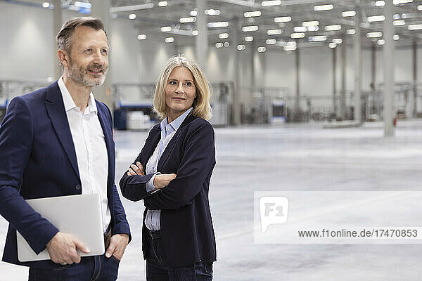 Male professional standing by female colleague with arms crossed in industry