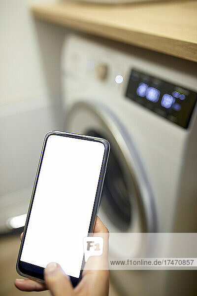 Frau benutzt Smartphone im Hauswirtschaftsraum zu Hause